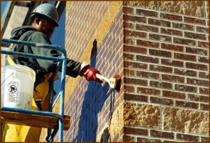 A worker gently scrubs a masonry wall. Gentle scrubbing is usually all that's needed if you're cleaning correctly. The masonry cleaner should do most of the work of dissolving contaminants. 